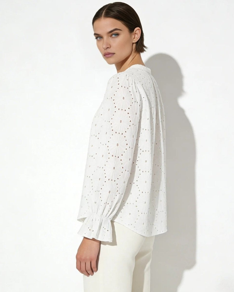 Side view of a model in a white long-sleeve eyelet blouse showing the relaxed fit and ruffled cuff detail.