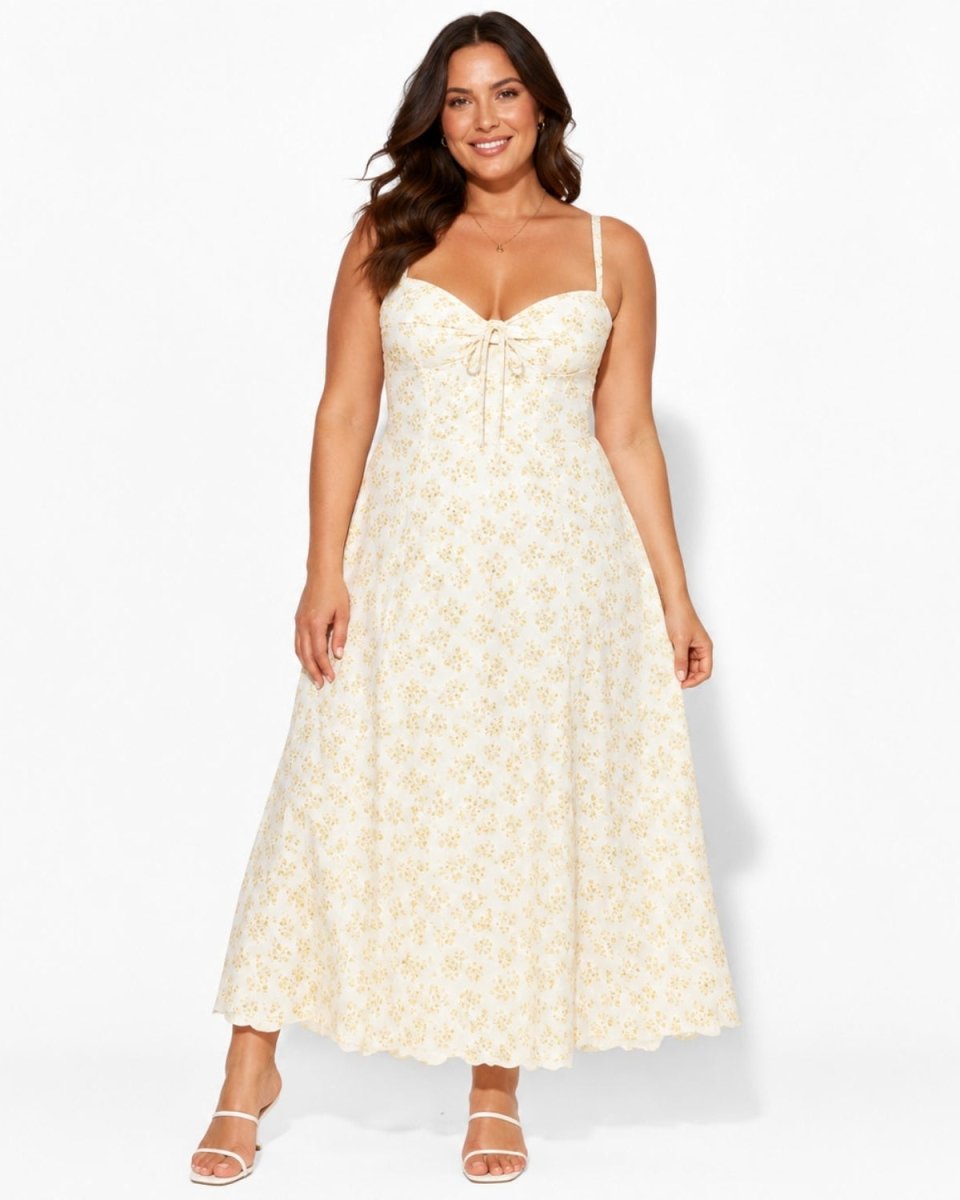 A woman modeling a cream maxi dress with a delicate yellow floral pattern and spaghetti straps against a plain white studio background.