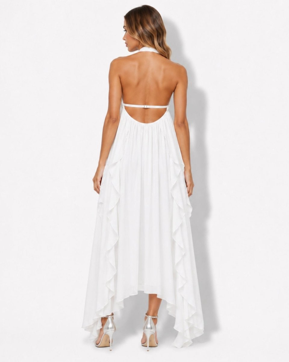 A woman modeling a white halter-neck maxi dress from the back, featuring a low open back, thin shoulder straps, and a high-low ruffled hemline, set against a plain white studio background.