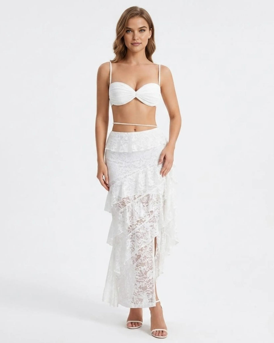 Front view of the white lace tiered ruffle maxi skirt and pearl strap bralette two piece set worn by a blonde model.