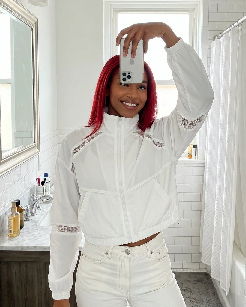 Lifestyle mirror selfie of a woman wearing the Kouvr white mesh activewear jacket with red hair