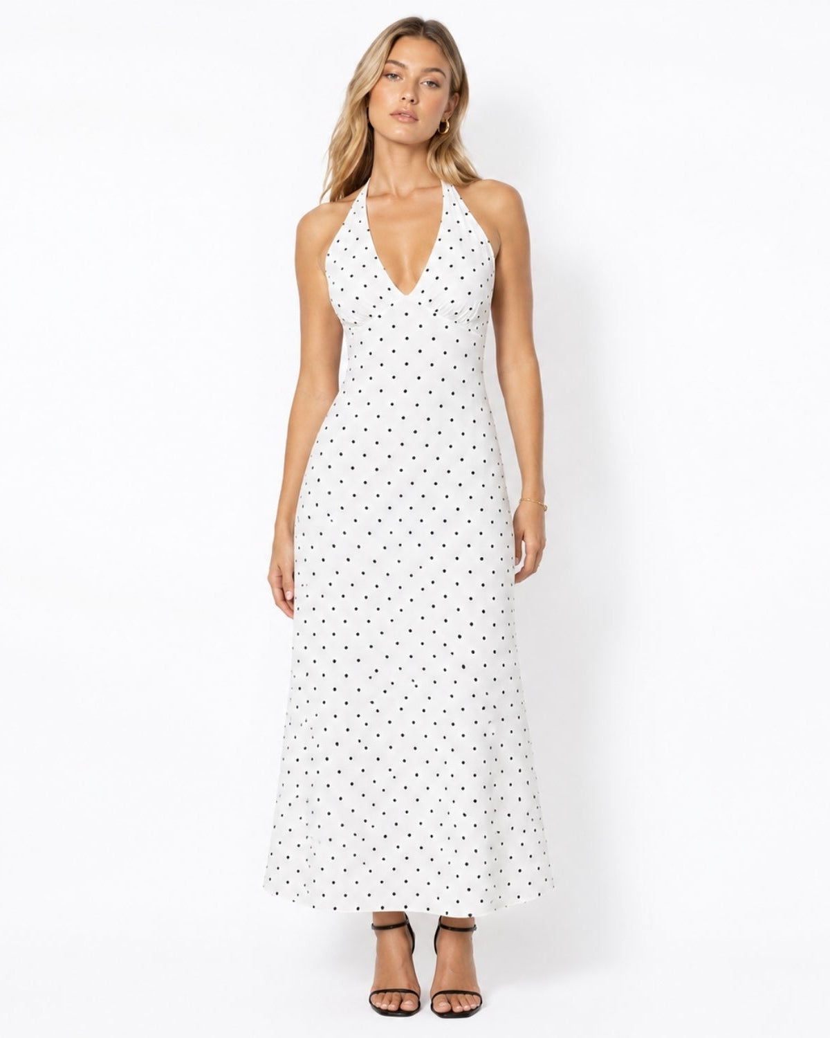 Woman wearing a luxury white and black polka dot halter neck midi dress with a V-neckline and ruched bust.
