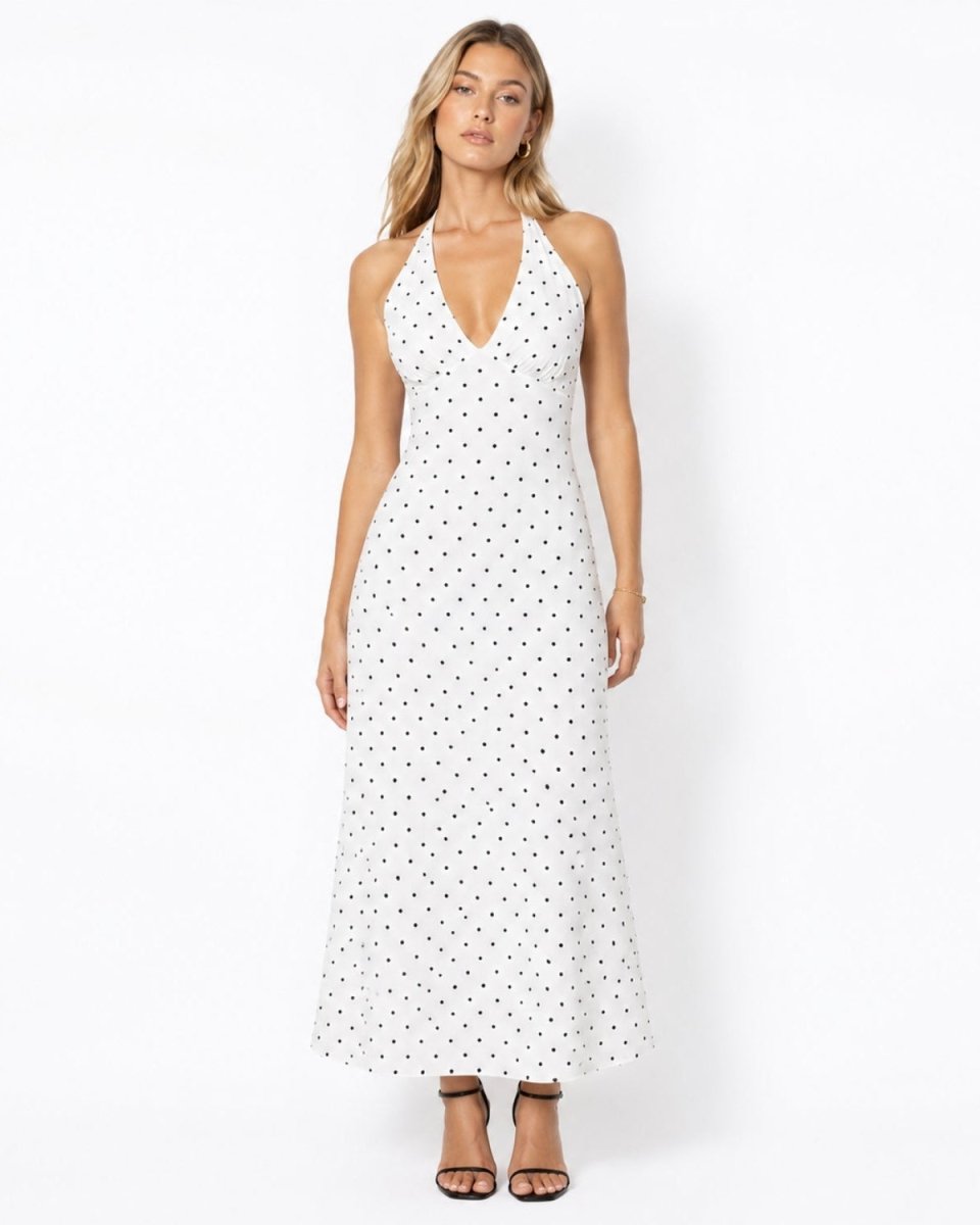 Woman wearing a luxury white and black polka dot halter neck midi dress with a V-neckline and ruched bust.