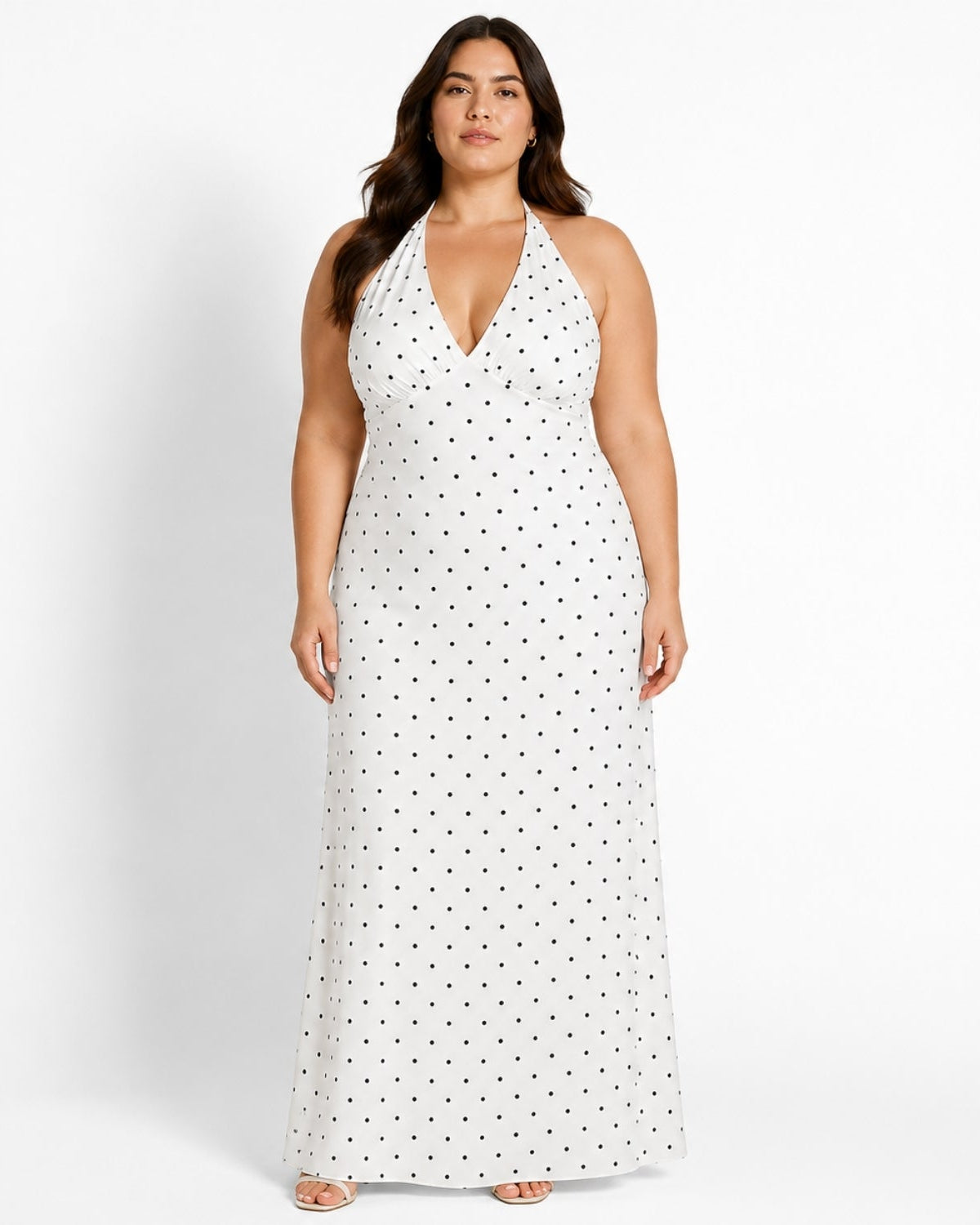 A woman modeling a white halter-neck maxi dress with a black polka dot pattern against a plain white studio background.