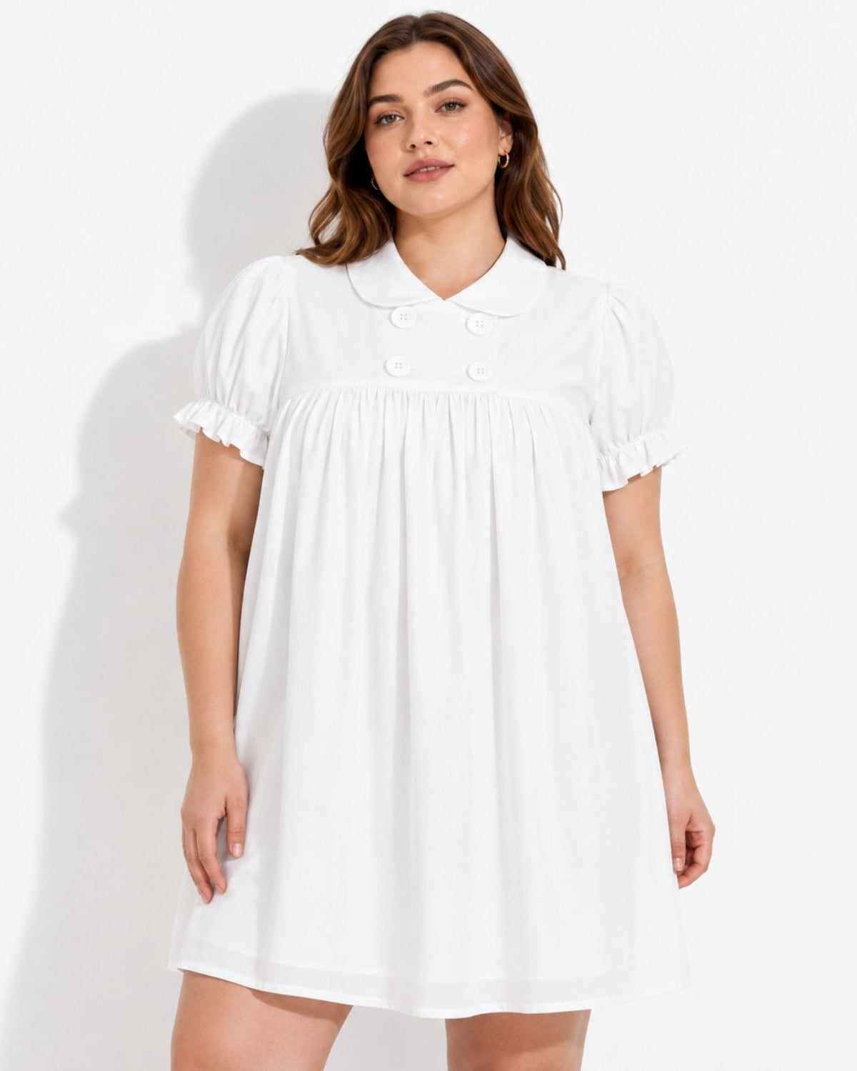 A woman modeling a white short-sleeve babydoll dress with a Peter Pan collar, double-button detail, and ruffled sleeves against a plain white studio background.