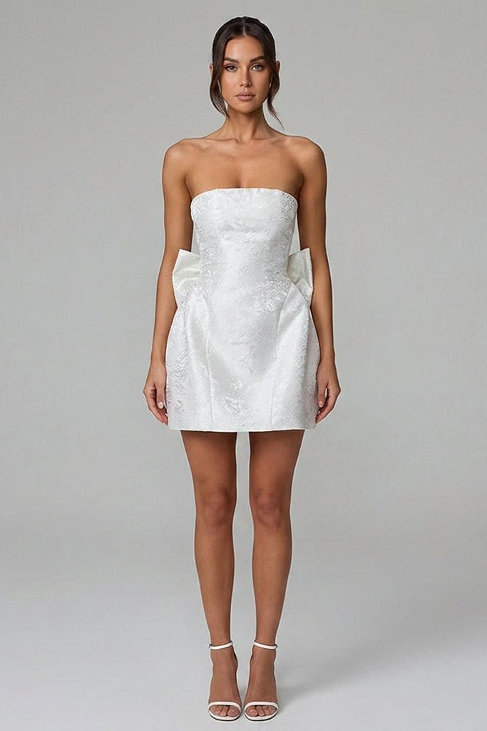 White strapless mini dress with subtle floral jacquard pattern worn by a brunette model facing forward