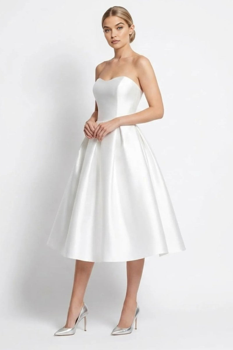 Side angle view of woman modeling a white strapless sweetheart midi dress in satin finish.