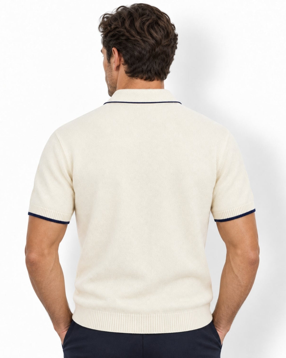 A man viewed from the back wearing a white-colored short-sleeve knit polo shirt with navy blue trim on the collar and sleeve cuffs, paired with dark navy trousers, against a clean white background.