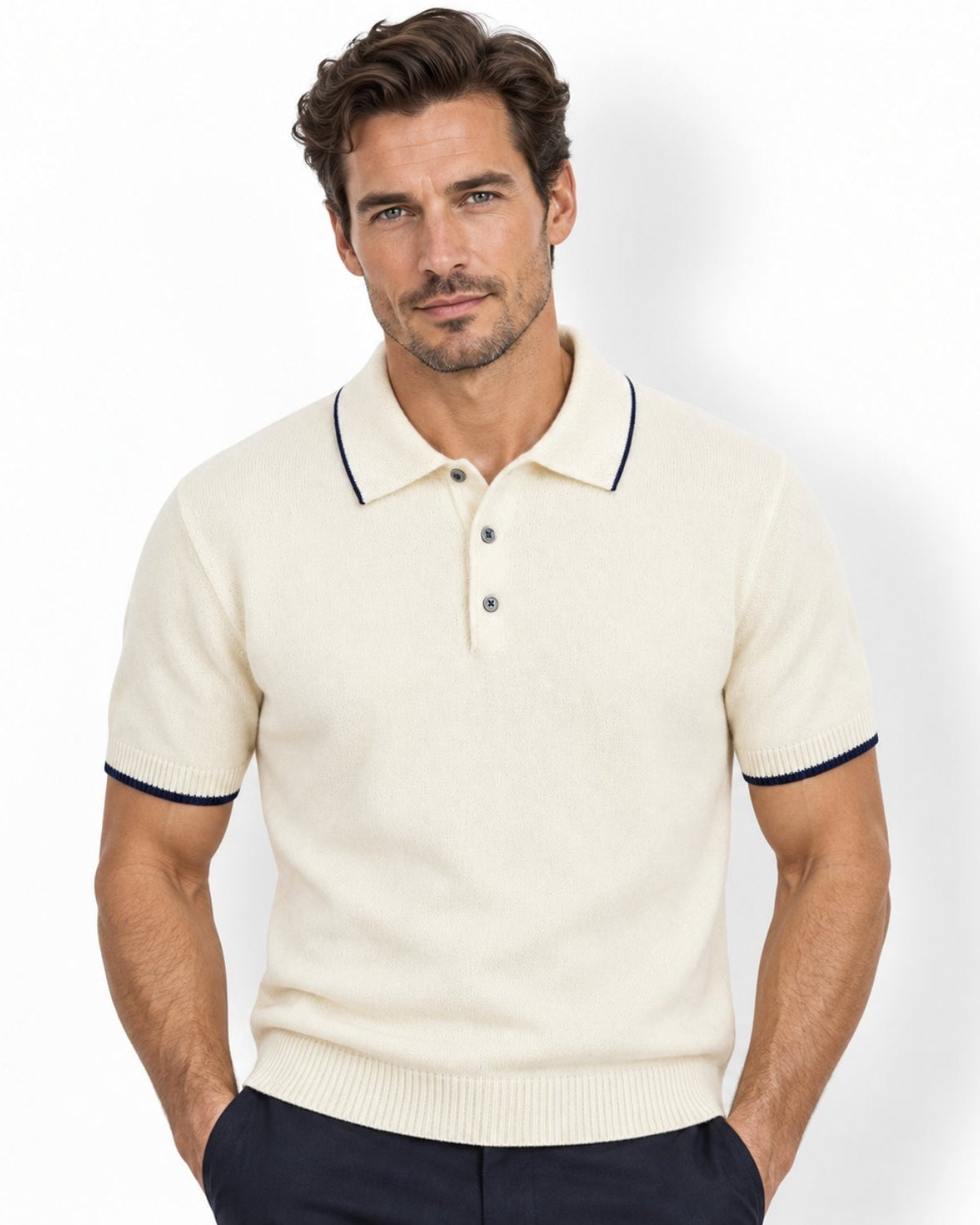 A man wearing a white-colored short-sleeve knit polo shirt with navy blue trim on the collar and sleeve cuffs, paired with dark trousers, against a plain white background.
