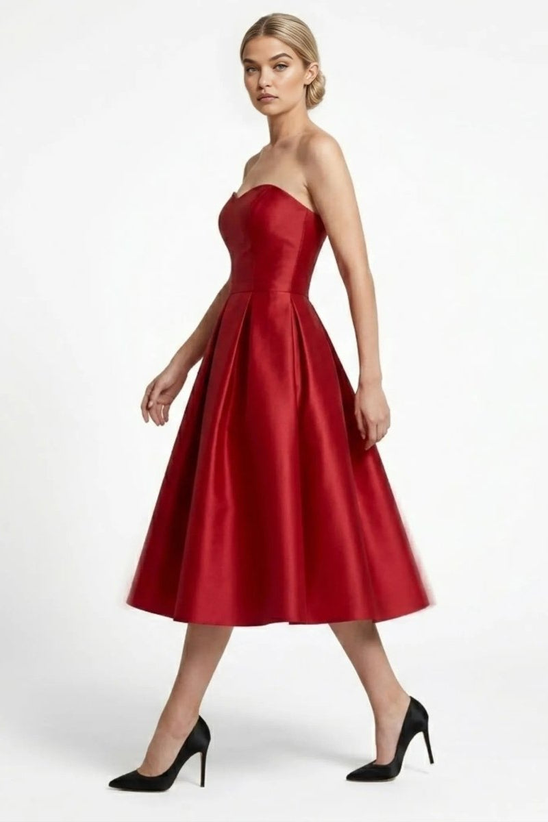 Side profile view of walking model in elegant wine red strapless A-line midi party dress with structured pleated skirt