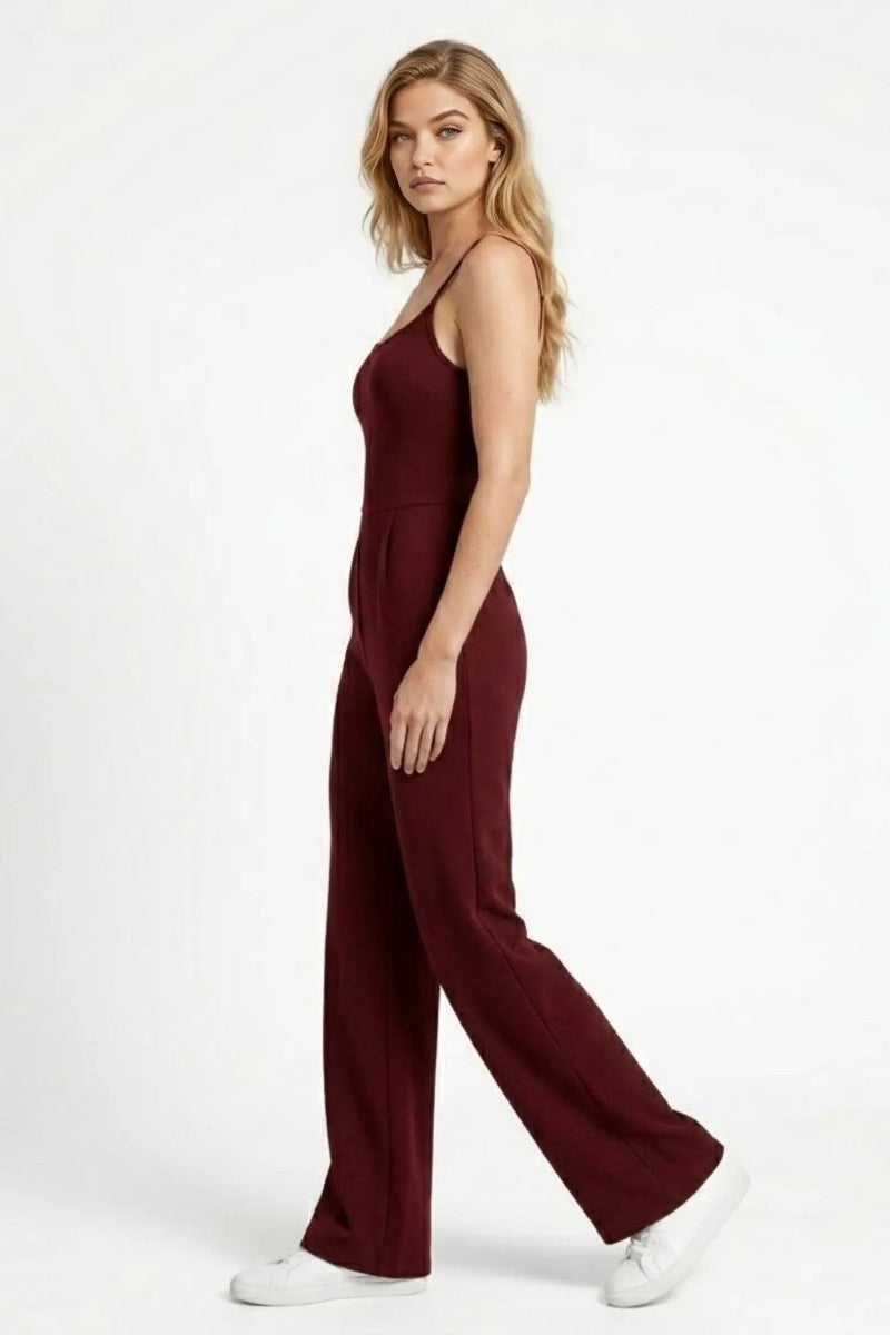 Side profile of woman walking in Fenlo Form wine red wide leg strappy jumpsuit showing fluid drape and fit.