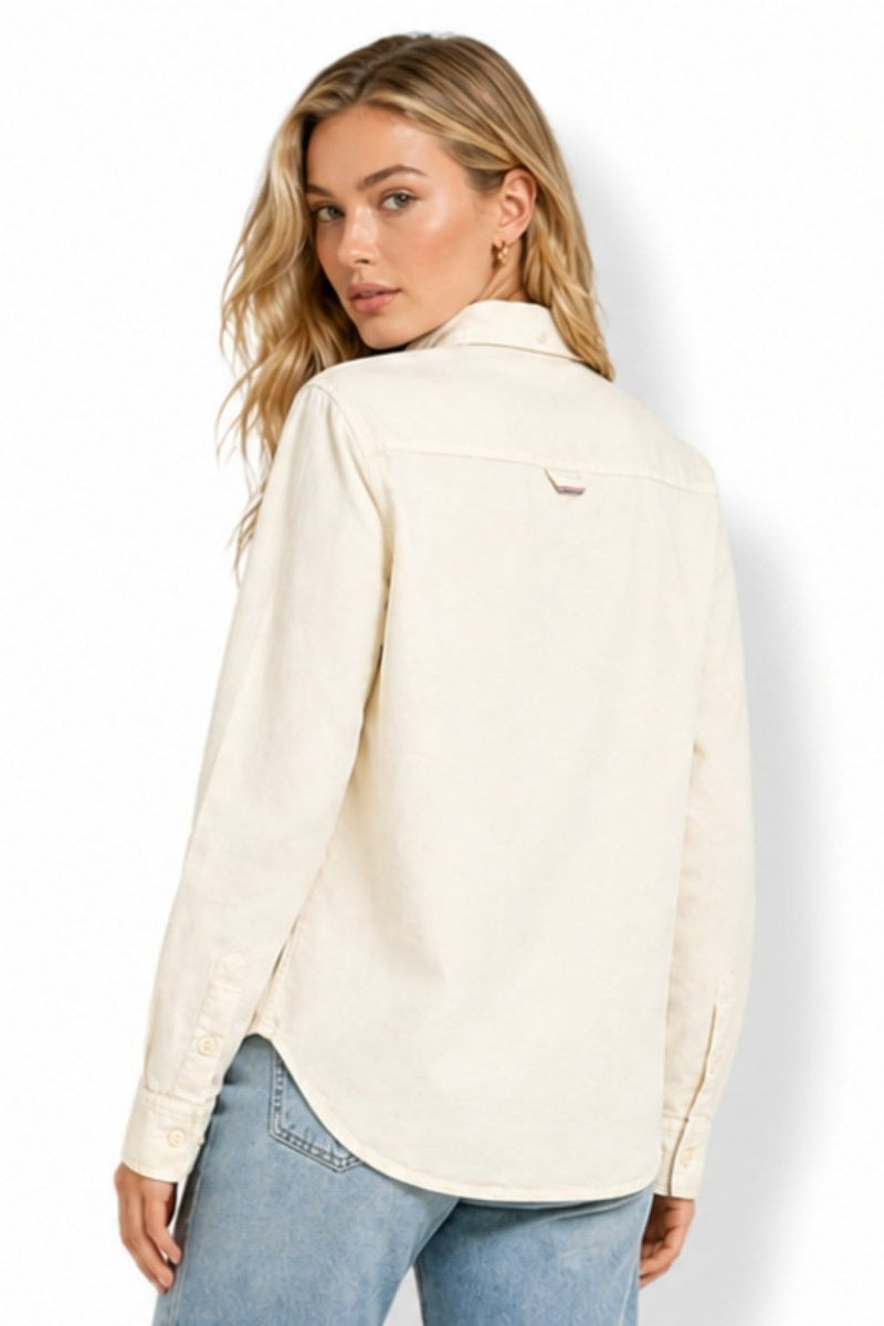 Back view of a women's beige cotton shacket highlighting the curved hemline, structured upper yoke, and subtle loop tag detail.