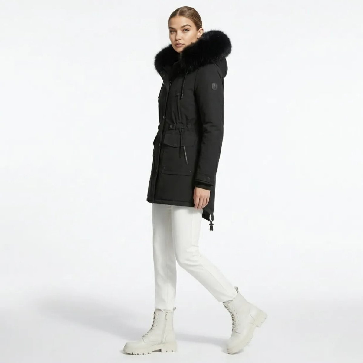 Side profile of a woman wearing a tailored black winter parka with plush black faux fur hood, walking forward.