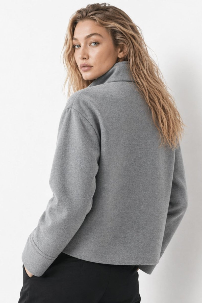Back view of a female model wearing a structured grey short coat with relaxed fit over black pants.