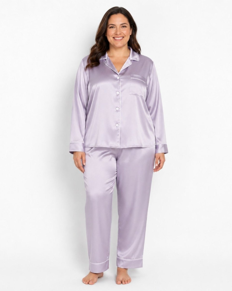 A woman modeling a two-piece lavender satin pajama set, featuring a long-sleeve button-up shirt and matching pants, against a plain white studio background.