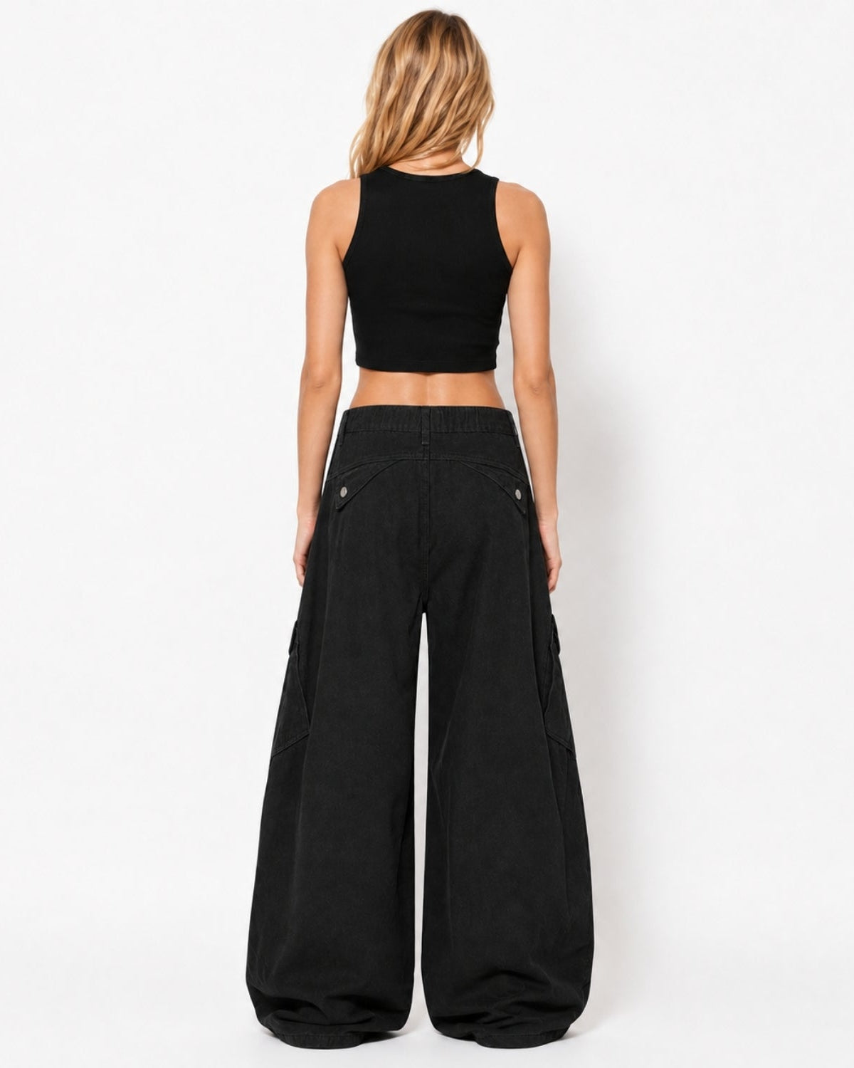 A woman viewed from the back wearing a black sleeveless crop top and very wide-leg black pants against a plain white studio background.