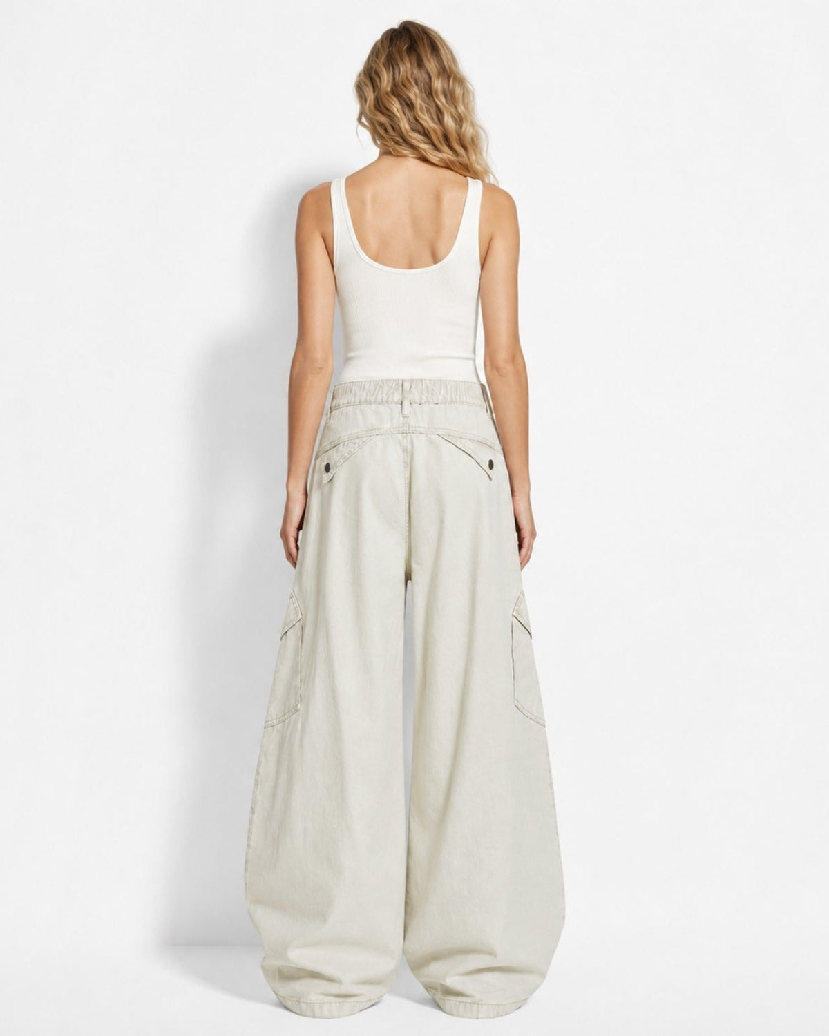 A woman shown from the back wearing a white ribbed tank top and light beige wide-leg cargo pants against a plain white studio background.