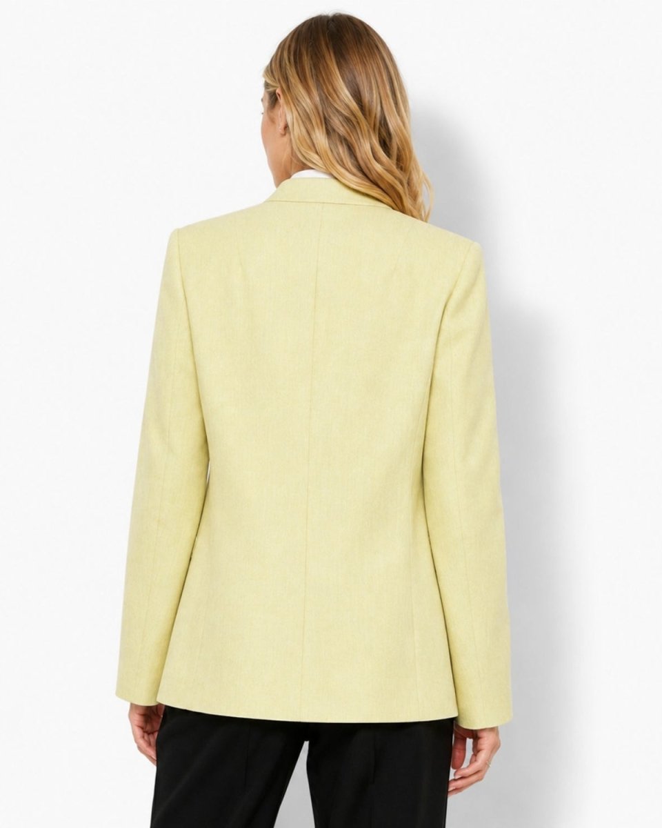 A woman shown from the back wearing a pale yellow blazer and black pants against a clean white studio background.