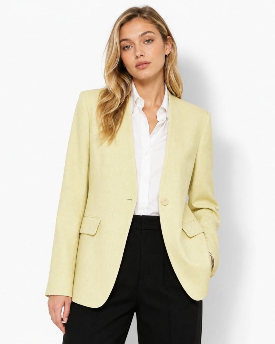 A woman modeling a pale yellow blazer over a white collared shirt and black trousers, photographed against a clean white studio background.