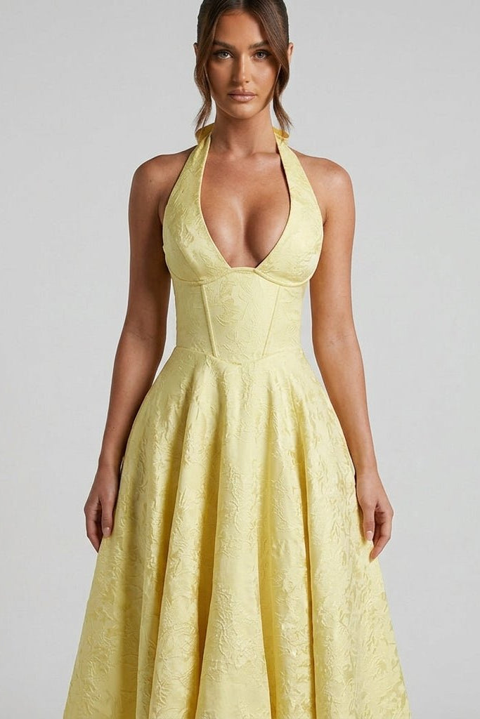 Close up of the structured corset bodice, plunging neckline, and floral embossed texture on the Kouvr yellow halter dress.