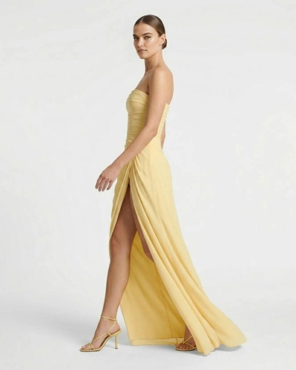 Side profile of fashion model in yellow corset back evening gown showing high leg slit and strappy heels.