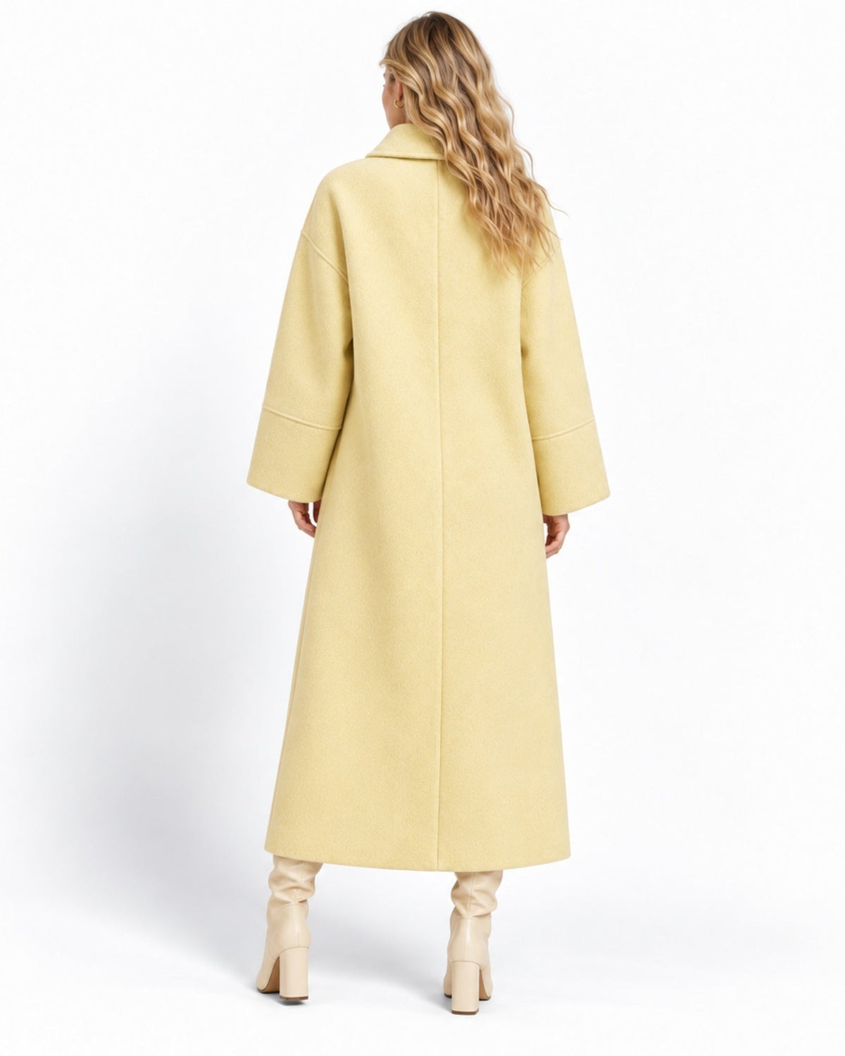 A woman viewed from behind wearing a long, light yellow coat and beige heeled boots against a plain white studio background.