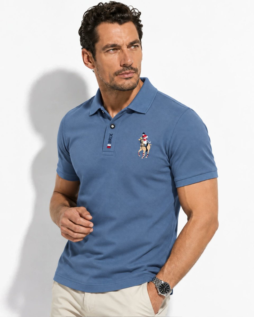 Brix: Model im blauen Poloshirt mit Brustmotiv und heller Hose vor hellem Hintergrund.
