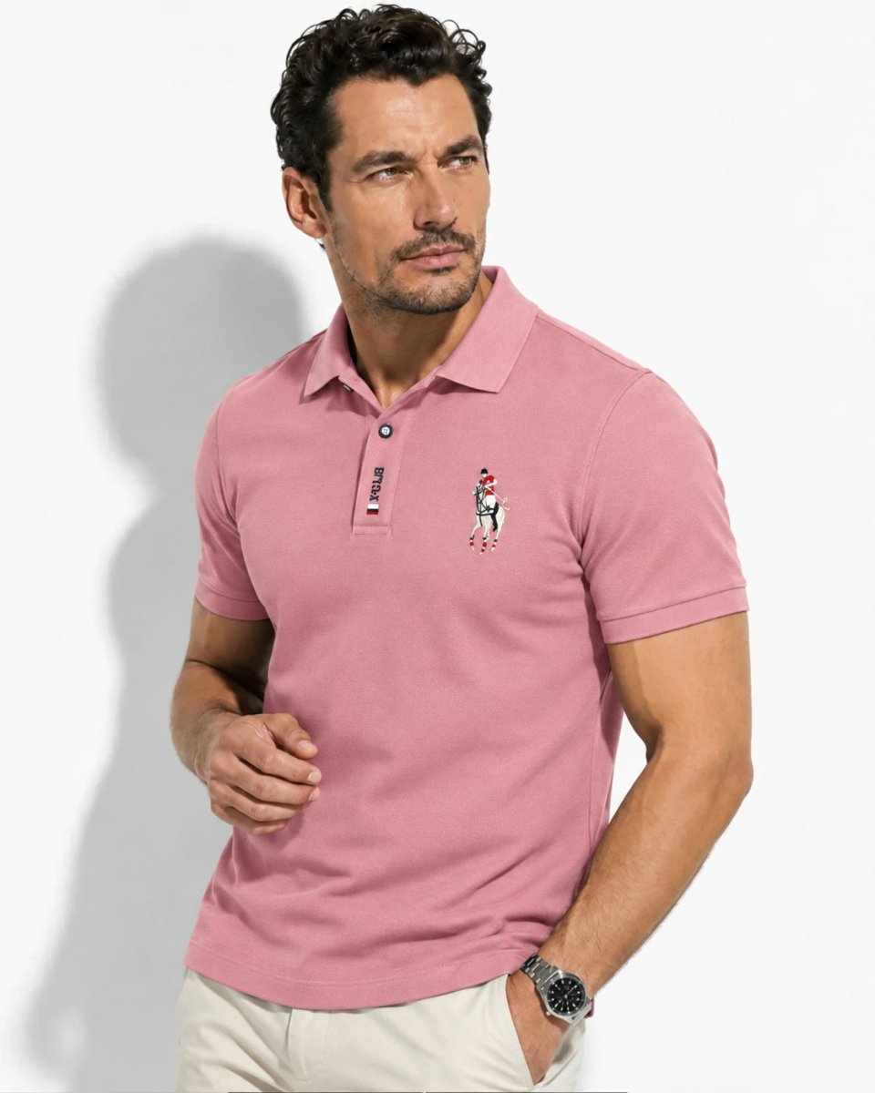 Brix: Model im rosafarbenen Poloshirt mit Brustmotiv und kurzer Knopfleiste vor hellem Hintergrund.