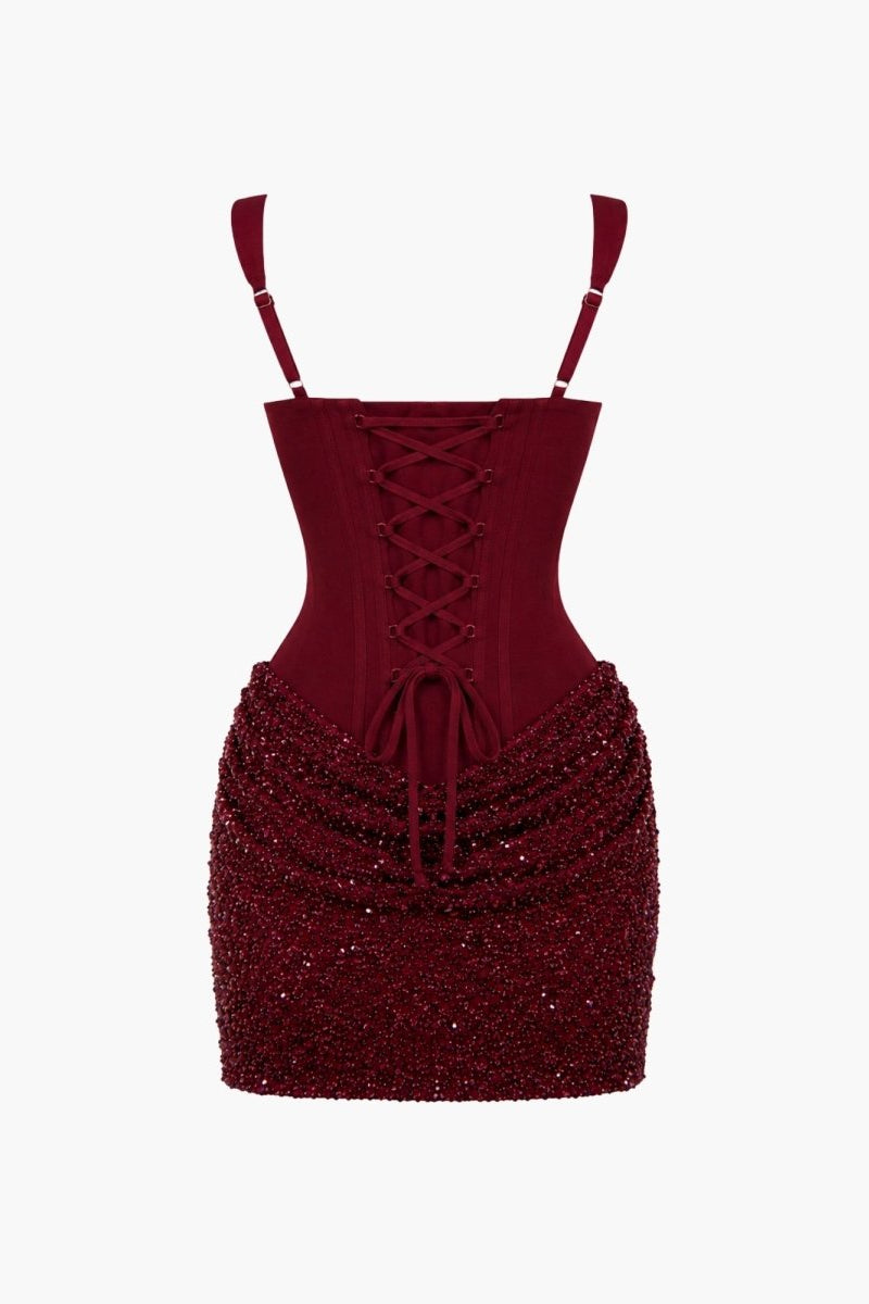 A deep burgundy sequined mini dress with a lace-up corset-style bodice and thin shoulder straps, shown against a plain white background.