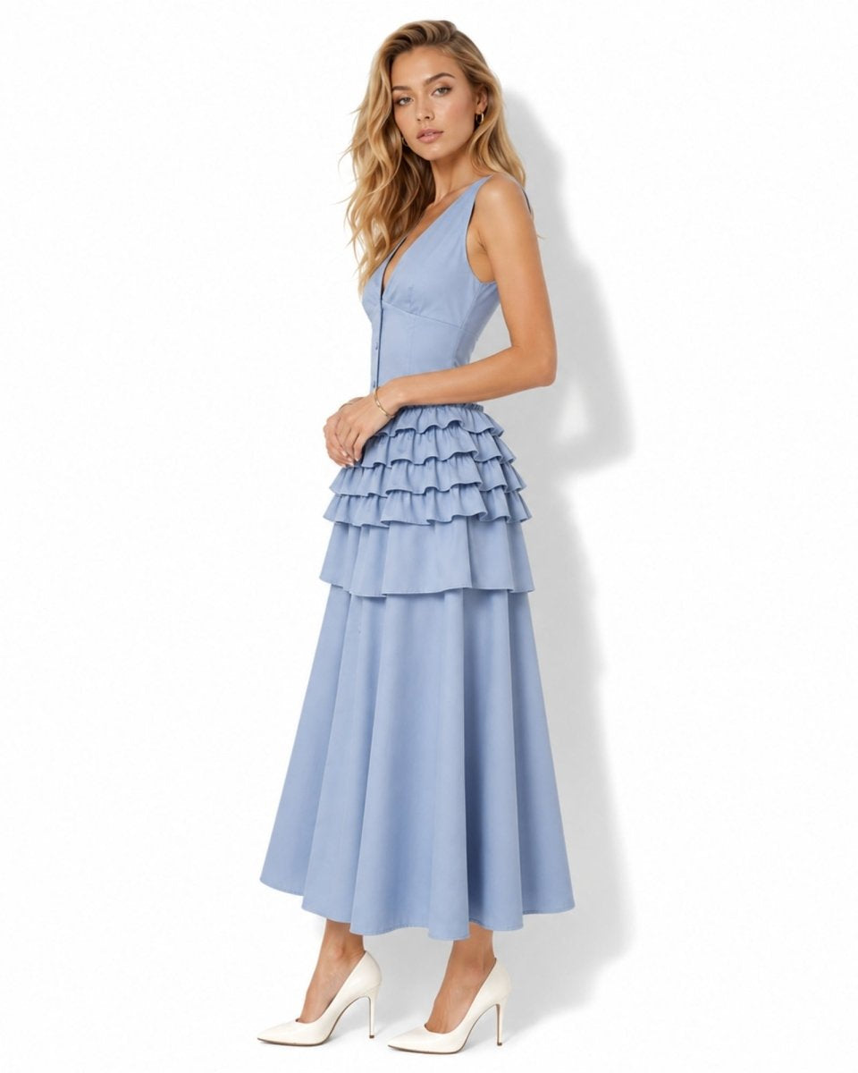 A woman modeling a sleeveless light blue maxi dress with a tiered ruffle skirt, paired with white pointed-toe heels, against a plain white background.