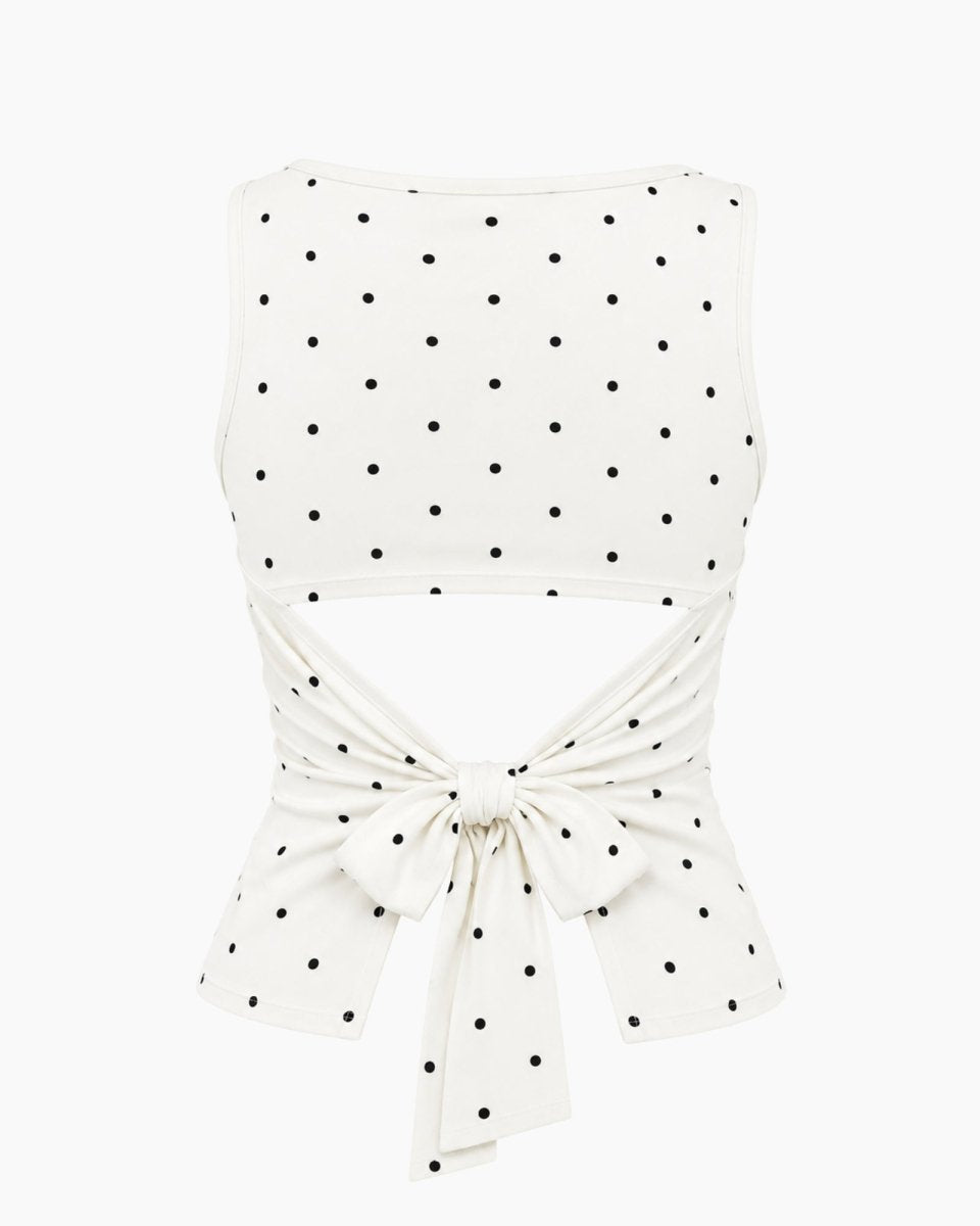 An off-white sleeveless crop top with a black polka dot pattern, featuring a tie-front waist design, shown against a plain white background.
