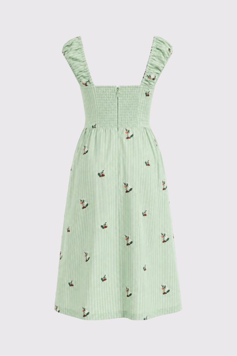 A light green pinafore dress with a smocked bodice, ruffled shoulder straps, and a small embroidered pattern of birds and flowers, shown on a neutral light gray background.