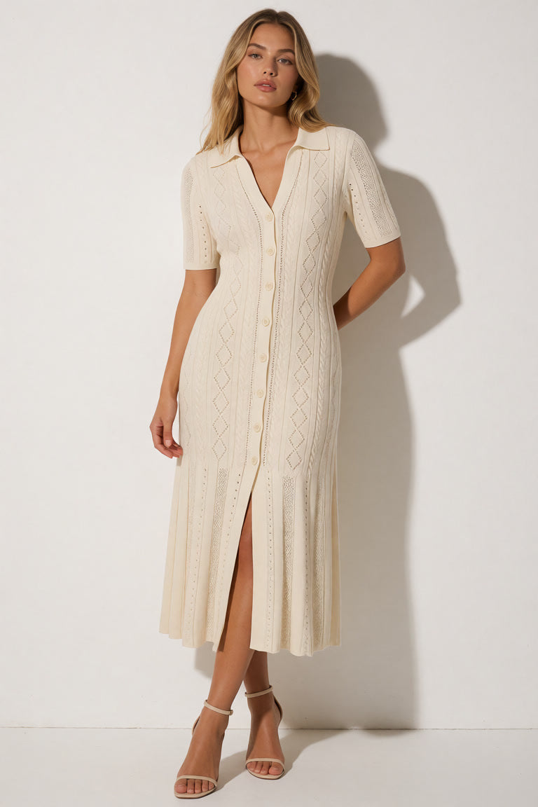 A woman models a cream-colored short-sleeve knit midi dress with a button-down front and a high leg slit, standing against a white wall with a soft shadow.