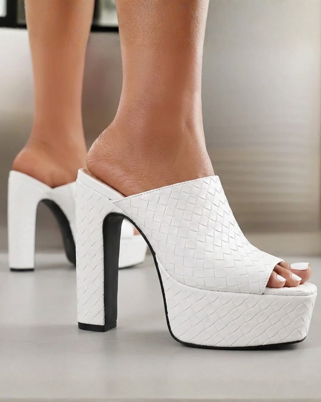 White woven-texture platform mule heels with high block heels, shown worn on a model's feet against a neutral indoor background.