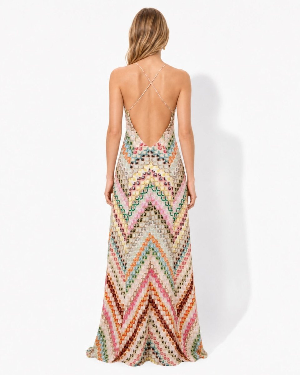 A woman viewed from the back wearing a sleeveless, open-back maxi dress with a multicolor chevron knit pattern on a plain white studio background.