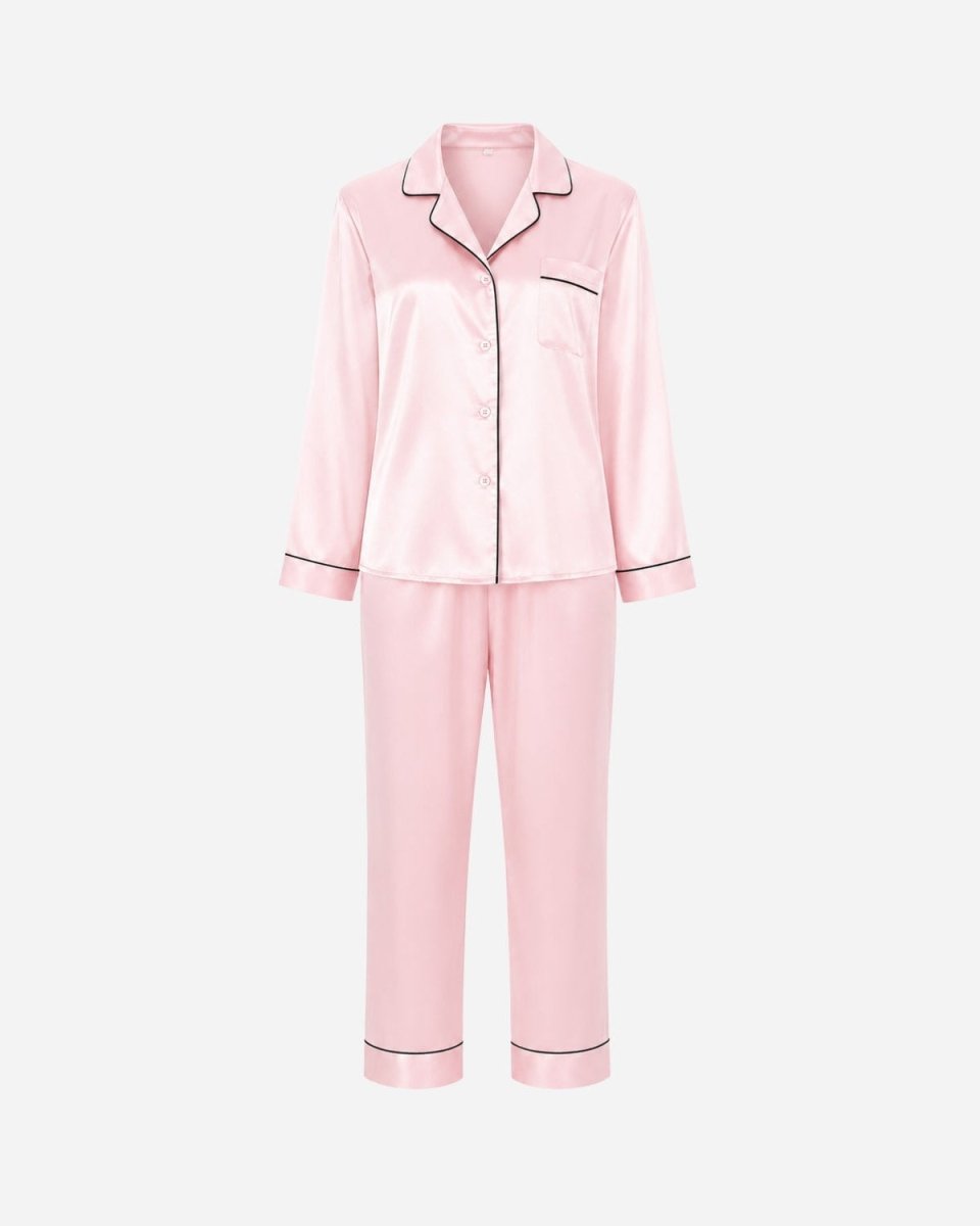 A two-piece pink satin pajama set with black piping trim, including a long-sleeve button-up top and matching pants, displayed on a clean white background.