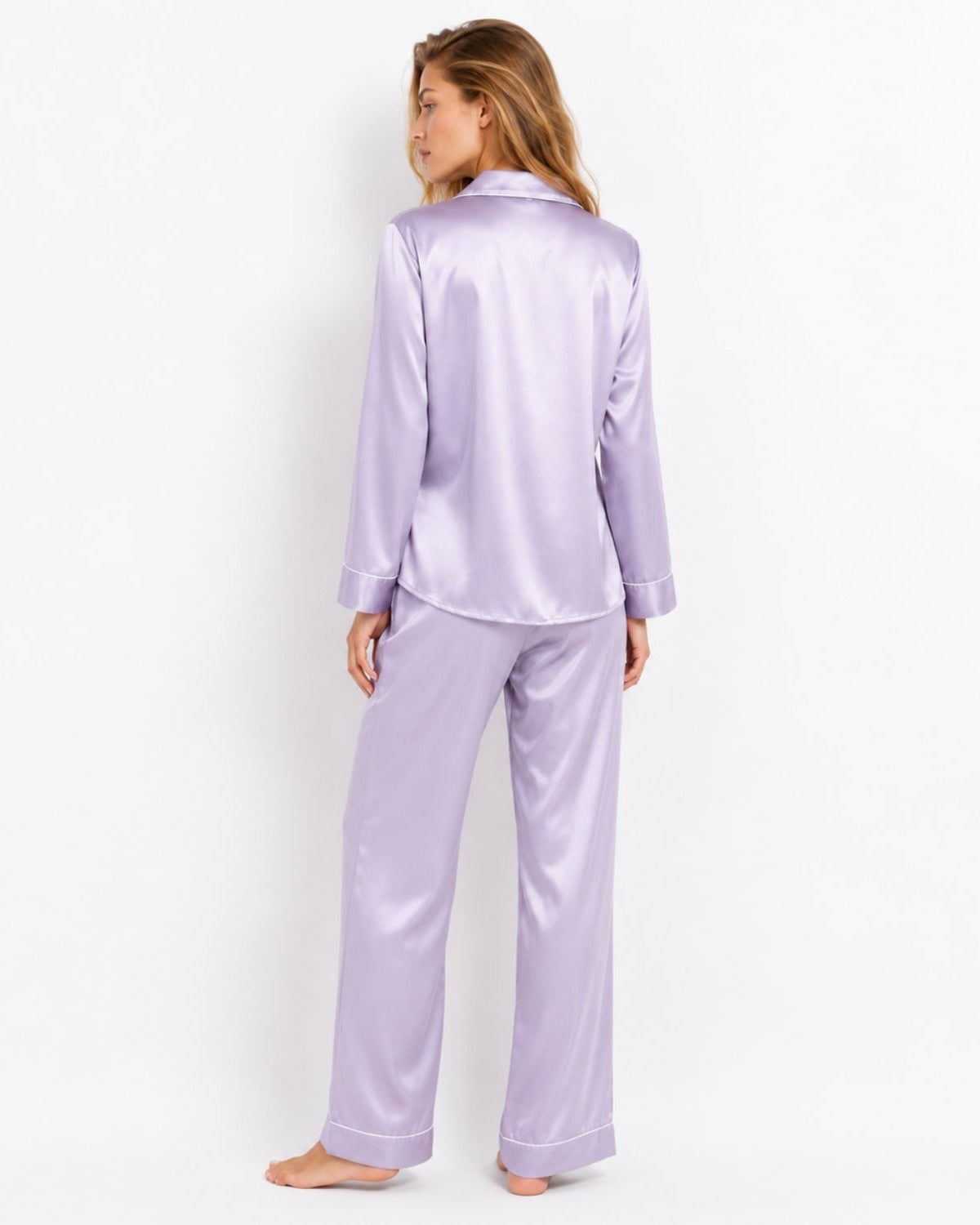 A woman wearing a lavender satin pajama set, viewed from the back, standing against a plain white studio background.