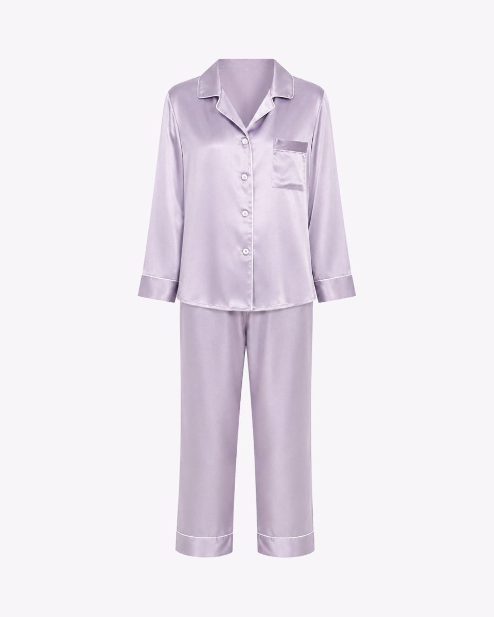 A two-piece women's pajama set in a light lavender satin fabric, featuring a long-sleeve button-up top with a collar and chest pocket, paired with matching wide-leg pants, shown against a plain white background.