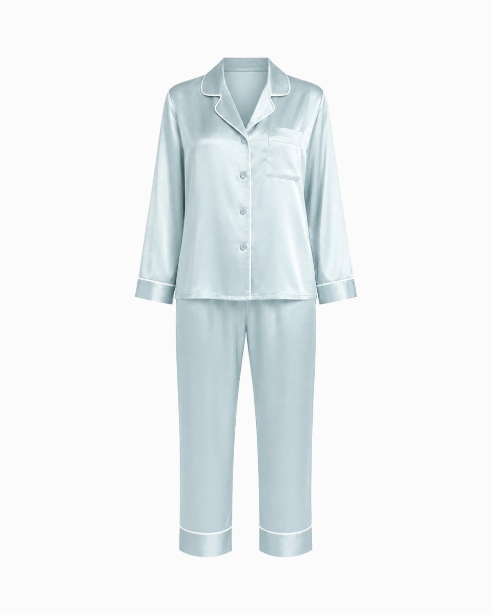 A light blue satin pajama set with a long-sleeve button-front top and matching pants, featuring white piping details, shown on a plain white background.