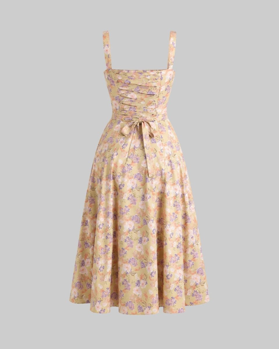 A sleeveless midi dress with thin shoulder straps, a gathered sweetheart bodice, and a matching waist tie, featuring a soft yellow-beige background with a purple and green floral pattern, shown against a solid gray background.