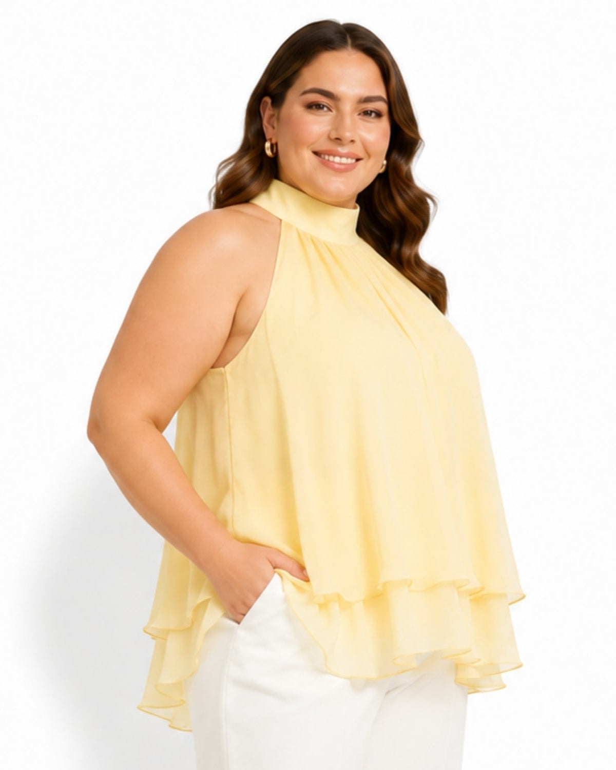 A woman modeling a pale yellow sleeveless high-neck ruffled blouse with white pants, photographed against a clean white studio background.
