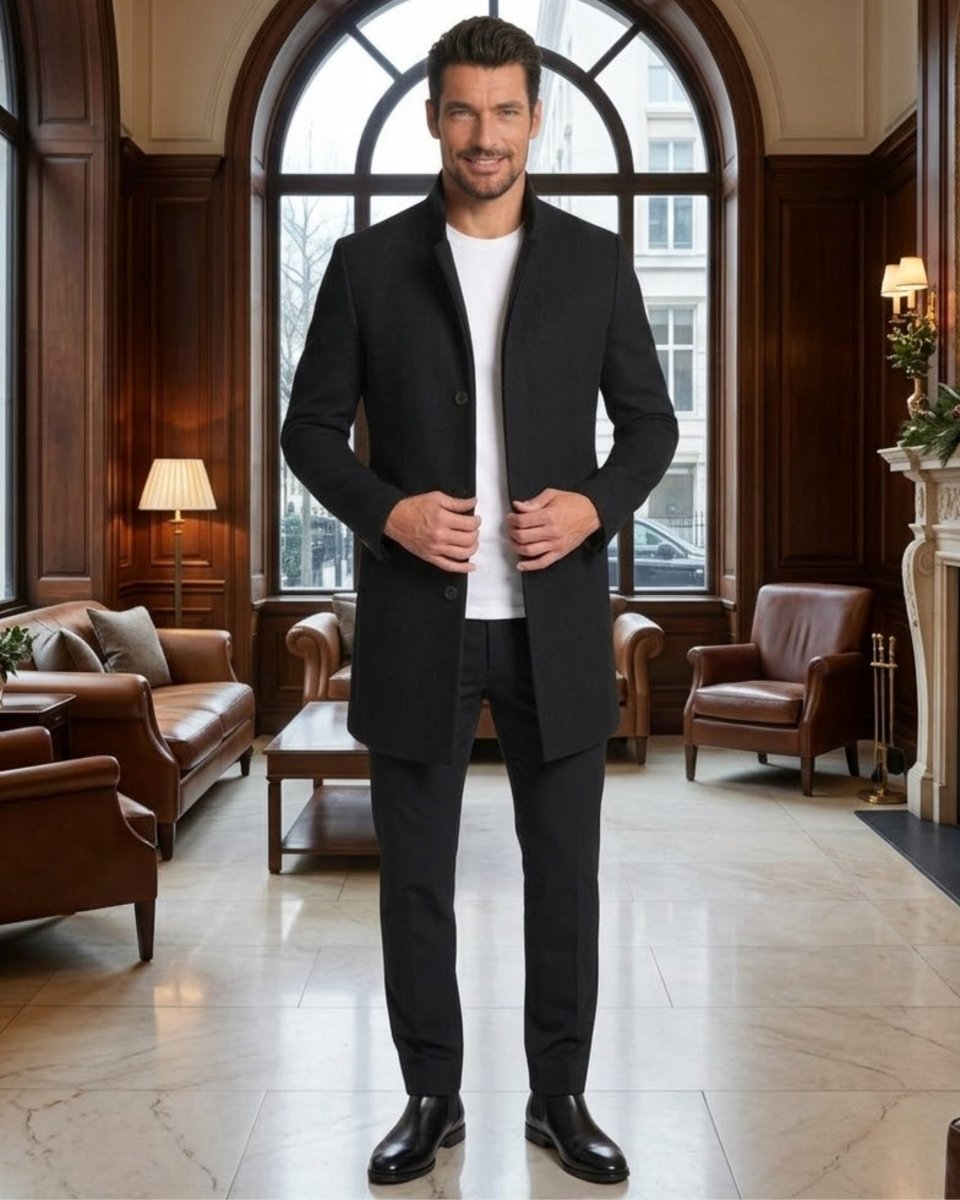 A man wearing a black overcoat, black trousers, and a white t-shirt stands in a luxurious, wood-paneled room with large arched windows.