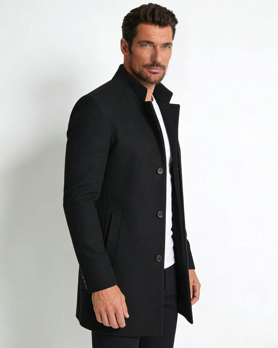 Side profile of a male model in a slim fit black wool overcoat, showing the tailored silhouette and mid-length cut.