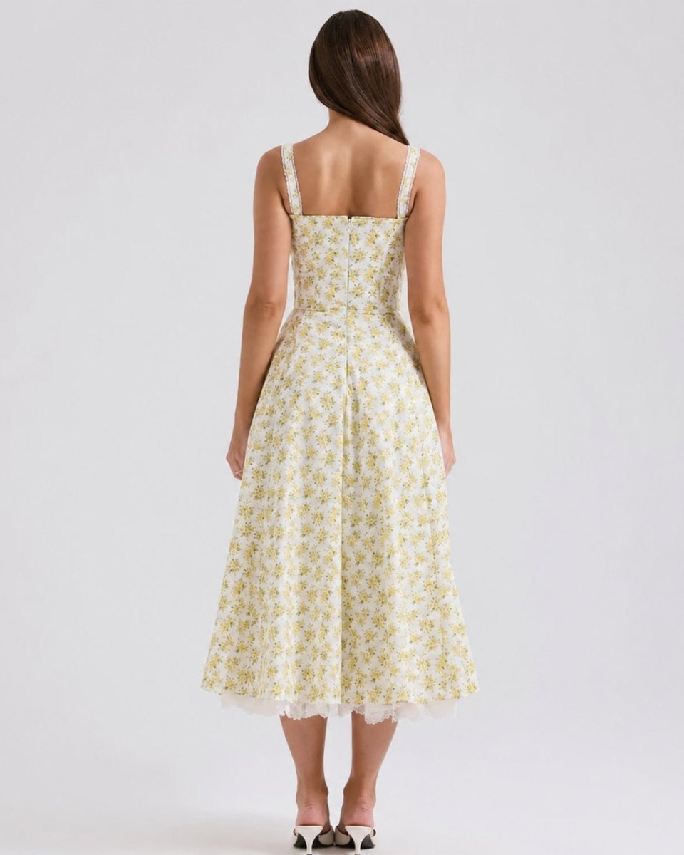 A woman viewed from the back wearing a sleeveless midi dress with a pale yellow and white floral print, photographed against a light gray studio background.