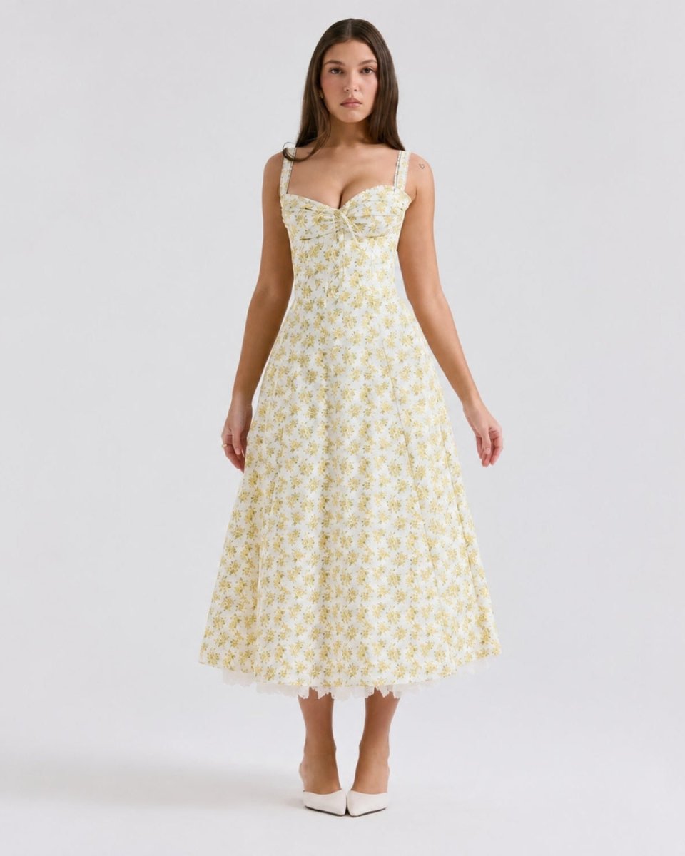 A woman modeling a sleeveless midi dress with a sweetheart neckline, thin straps, and a flared skirt. The dress has a pale yellow base with a small white floral pattern.