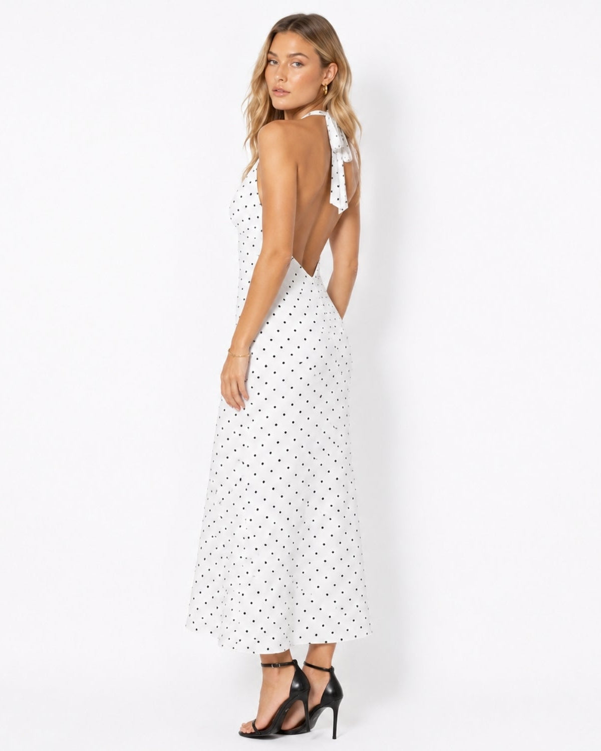 Side profile of a woman in an elegant open back white polka dot summer resort dress showing the fluid skirt drape.