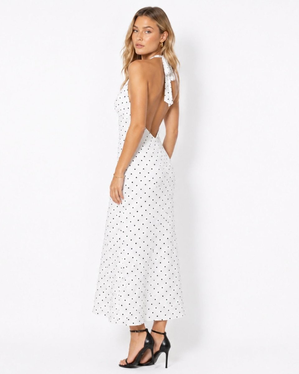 Side profile of a woman in an elegant open back white polka dot summer resort dress showing the fluid skirt drape.