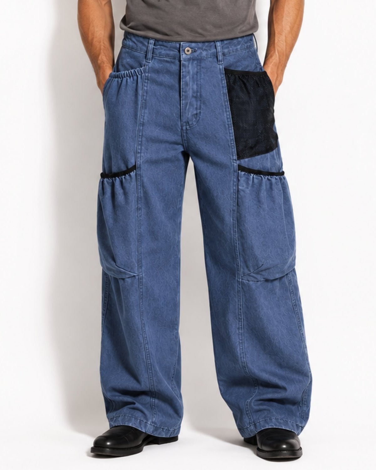 A person wearing wide-leg blue denim work pants with black contrast patch pockets and black trim, shown from the waist down against a plain white studio background.