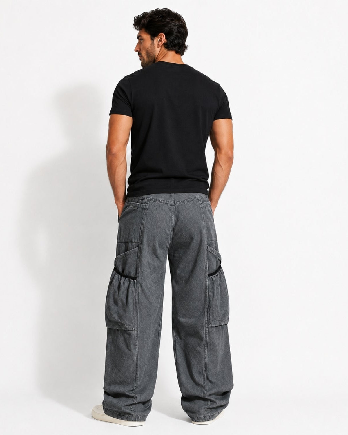 A man shown from the back wearing a black short-sleeve t-shirt and dark gray wide-leg cargo pants, standing against a plain white studio background.
