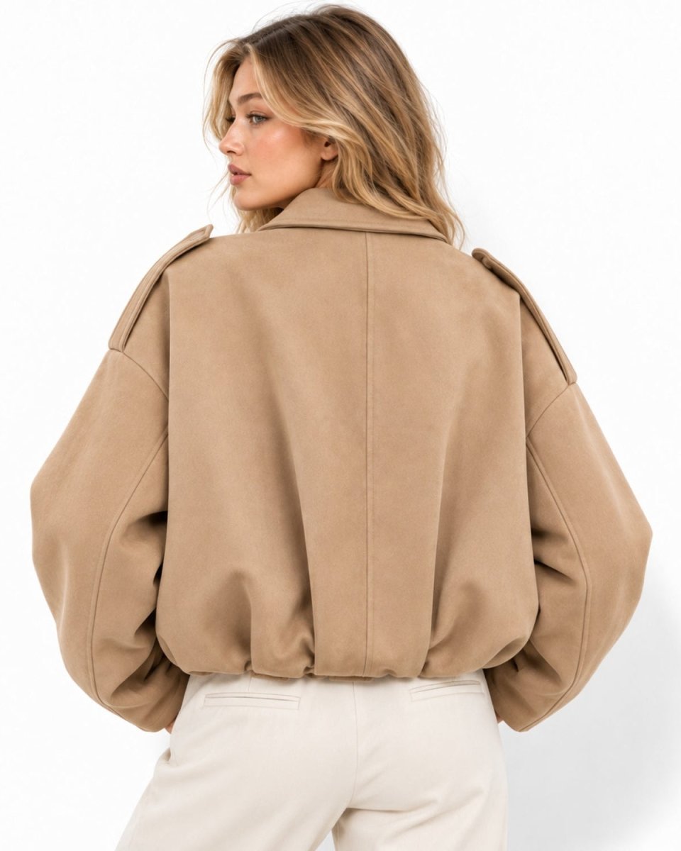 A woman shown from the back wearing a cropped camel-colored jacket with voluminous balloon sleeves and light cream pants, set against a plain white studio background.